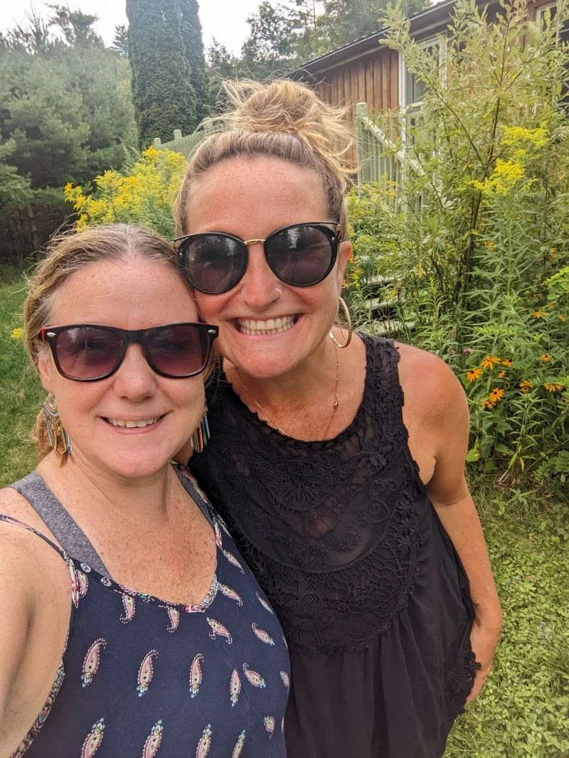 Cait &amp; Casey smiling at Raven Crest in front of flowering bushes