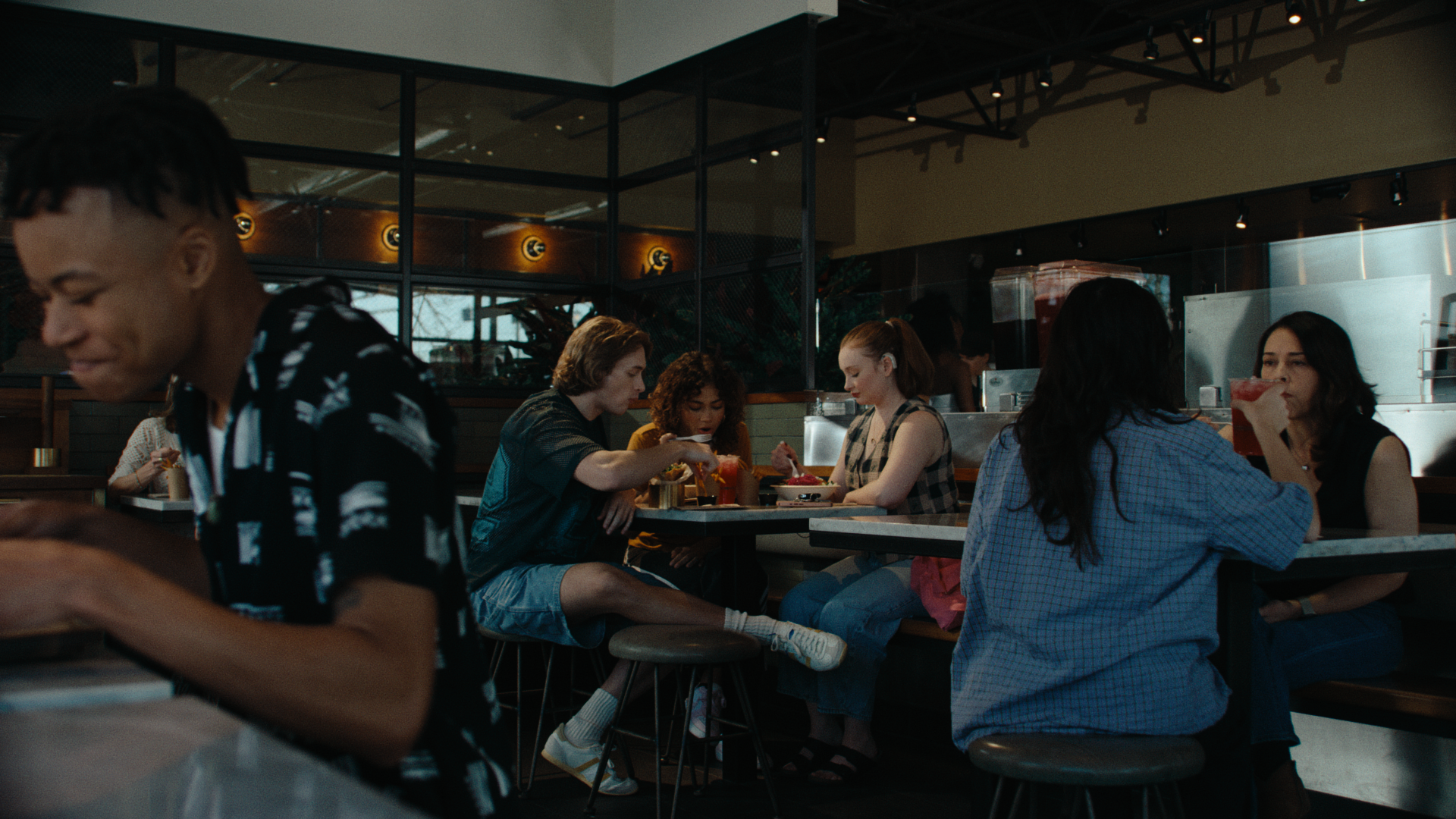 A group of friends sit at a table, eating, in a Brassica restaurant, surrounded by other patrons. The still is from "let's stay," a food commercial produced by waxpoet films, a commercial production company.