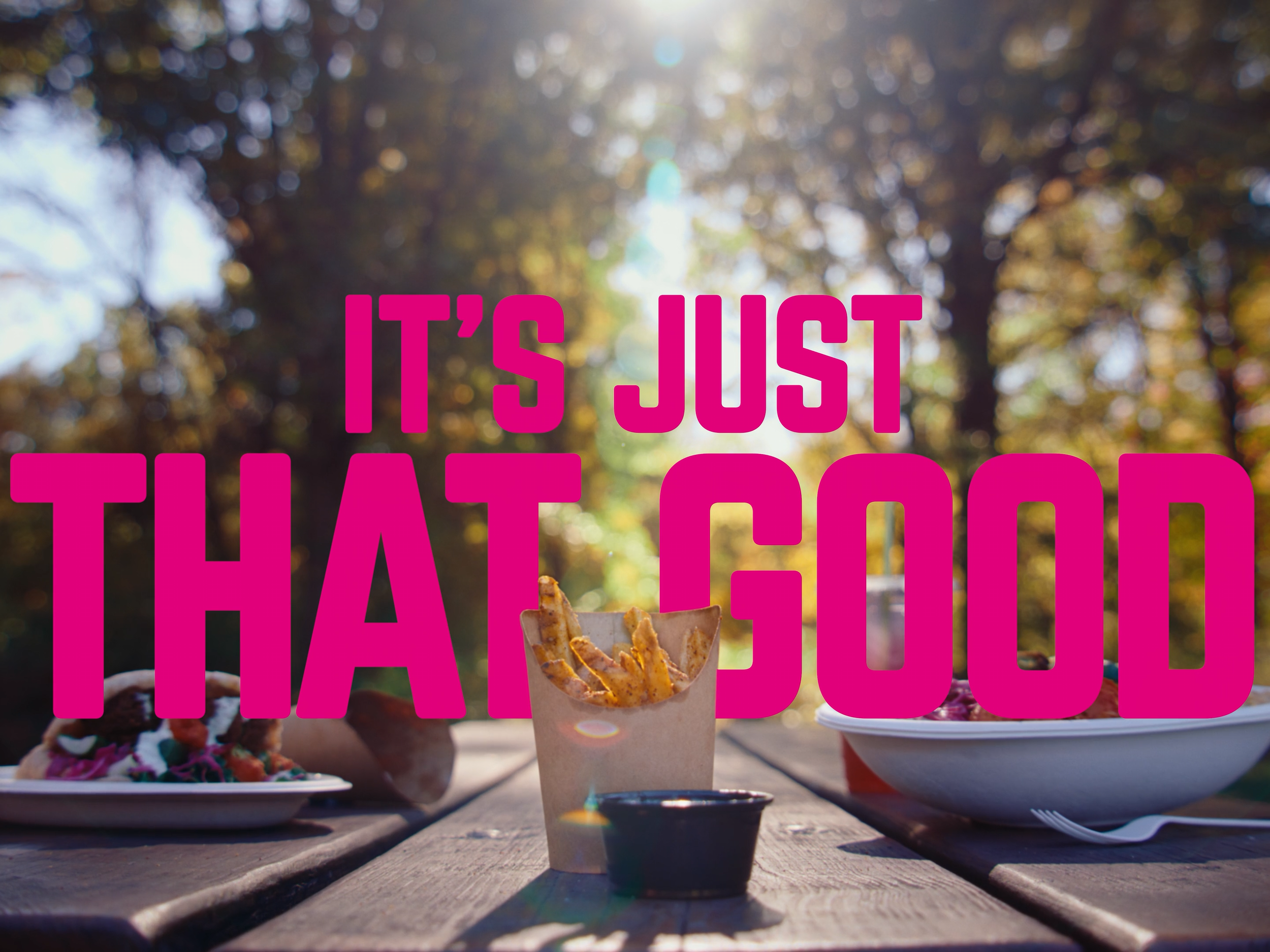 Pink on-screen text reads: "it's just that good." The text sits behind a small box of Brassica french fries. In the background is a Brassica pita sandwich and a Brassica salad. The still is from "just one more," a narrative commercial produced by com