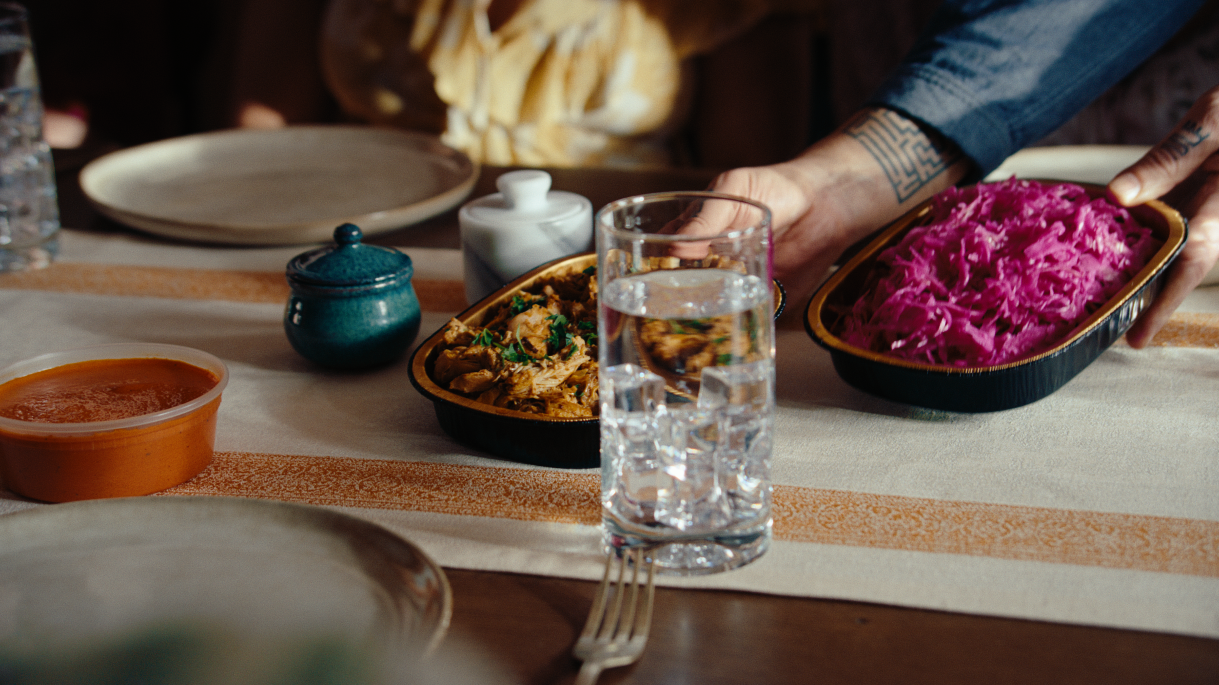 A close up of hands setting down dishes of Brassica chicken an pickled cabbage onto a dining table. The still is from "wow," a narrative food commercial produced by waxpoet, a production company based in Columbus, Ohio.
