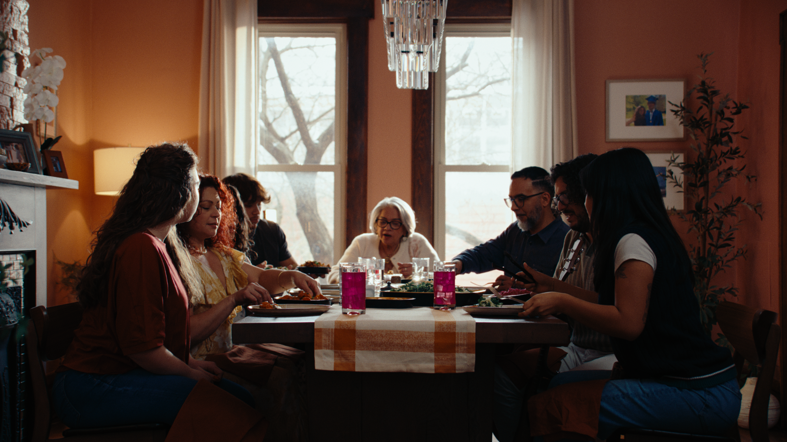 A family sits around a large dining table in a muted pink dining room, light streams in through windows as the family members dish food onto their plates. The still is from "wow," a narrative food commercial produced by waxpoet, a production company 
