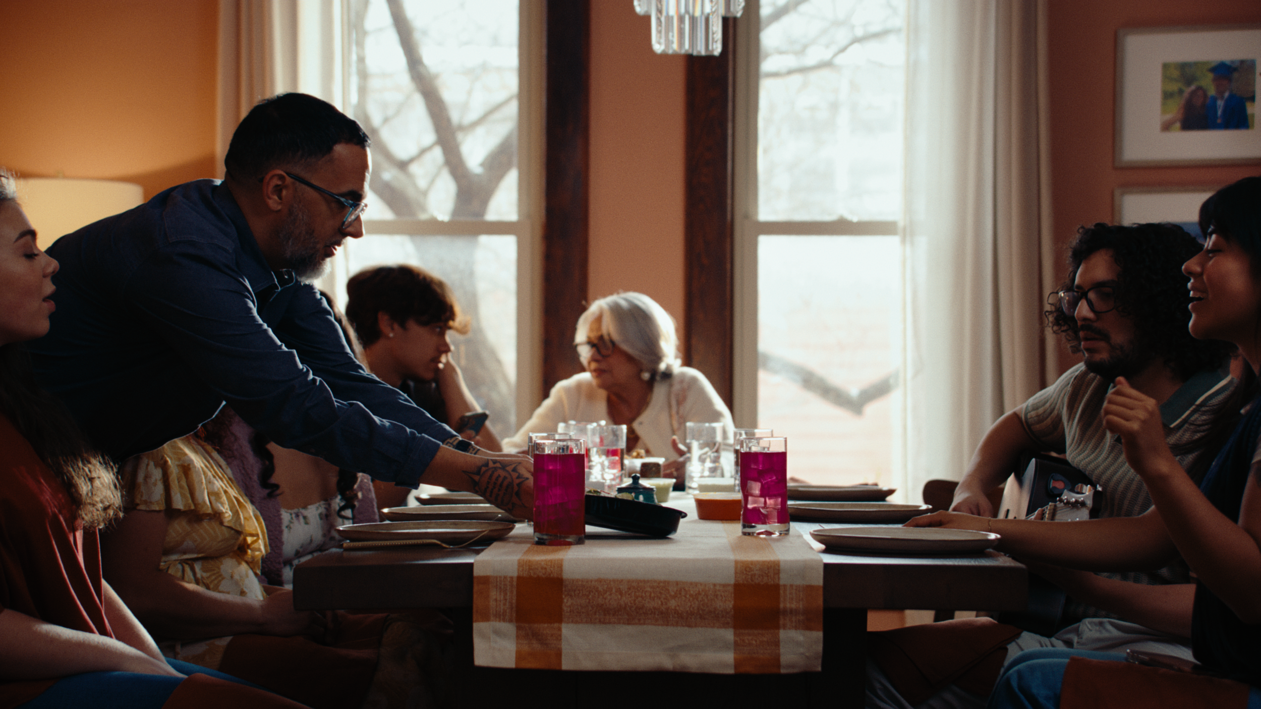 A family is gathered around a dining table set with drinks and dishes, a man sets down a dish of Brassica food onto the table. The still is from "wow," a narrative food commercial produced by waxpoet, a commercial production company.
