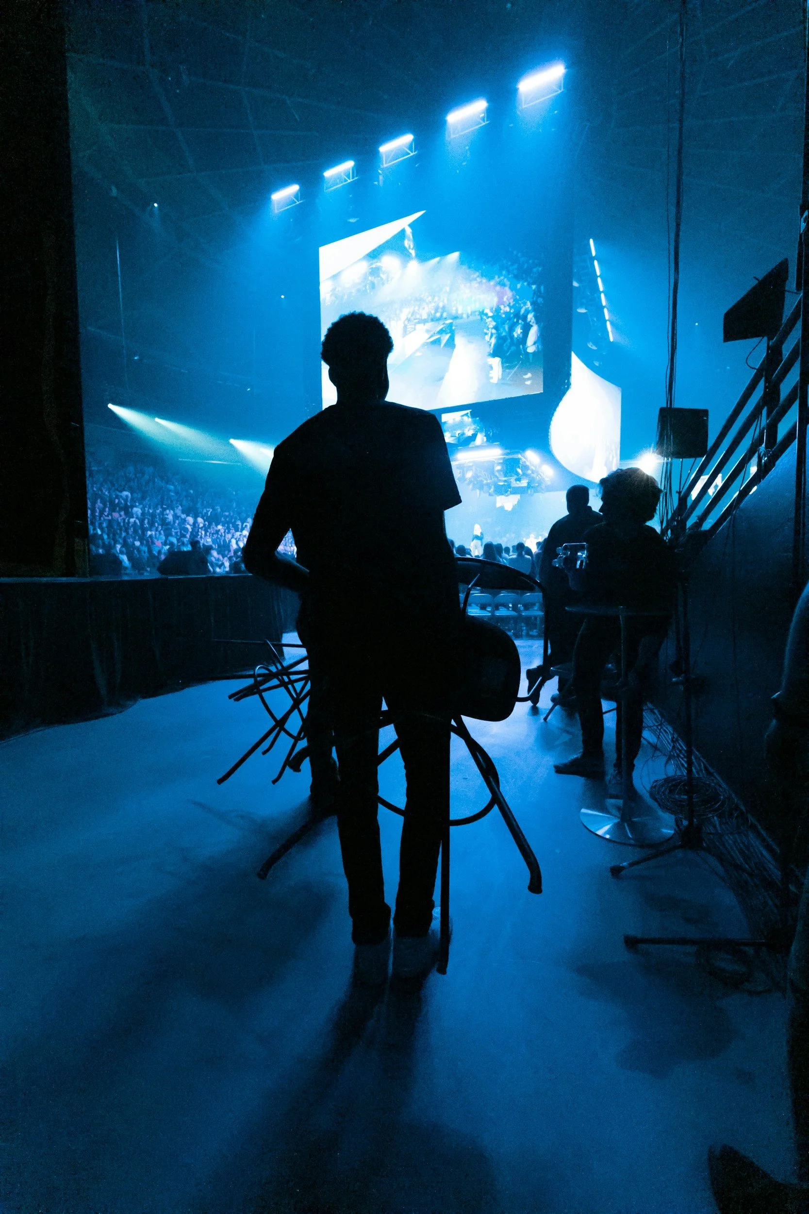 A person silhouetted by blue light carrying chairs.