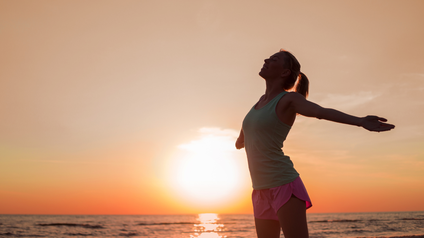 A carefree woman standing on the beach, looking at the sunset