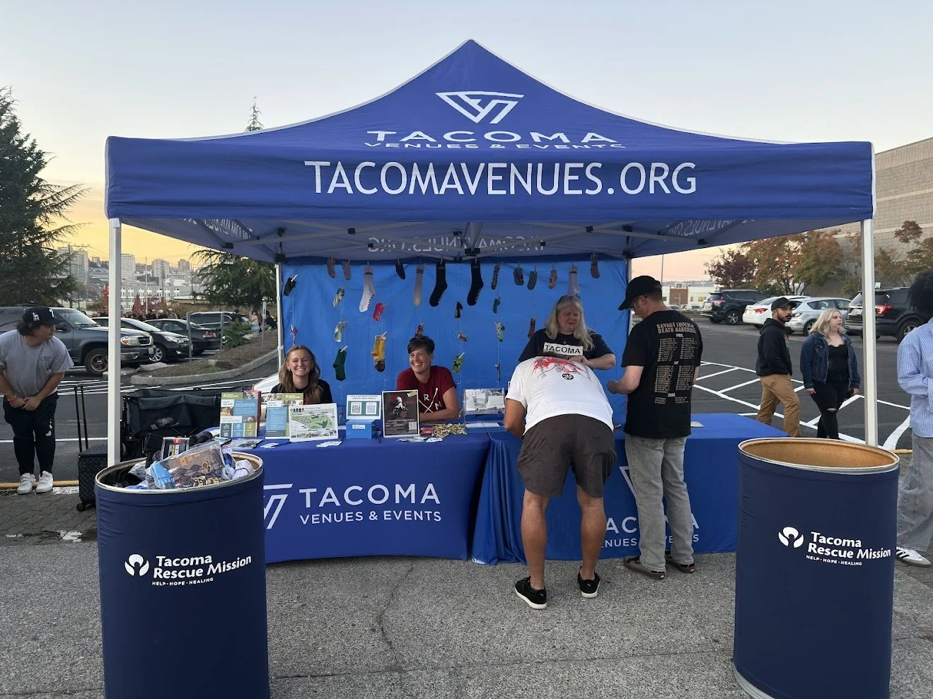Photo of a tent that has Tacoma Venues & Events with tabling outside the Tacoma Dome, with bins for sock donations