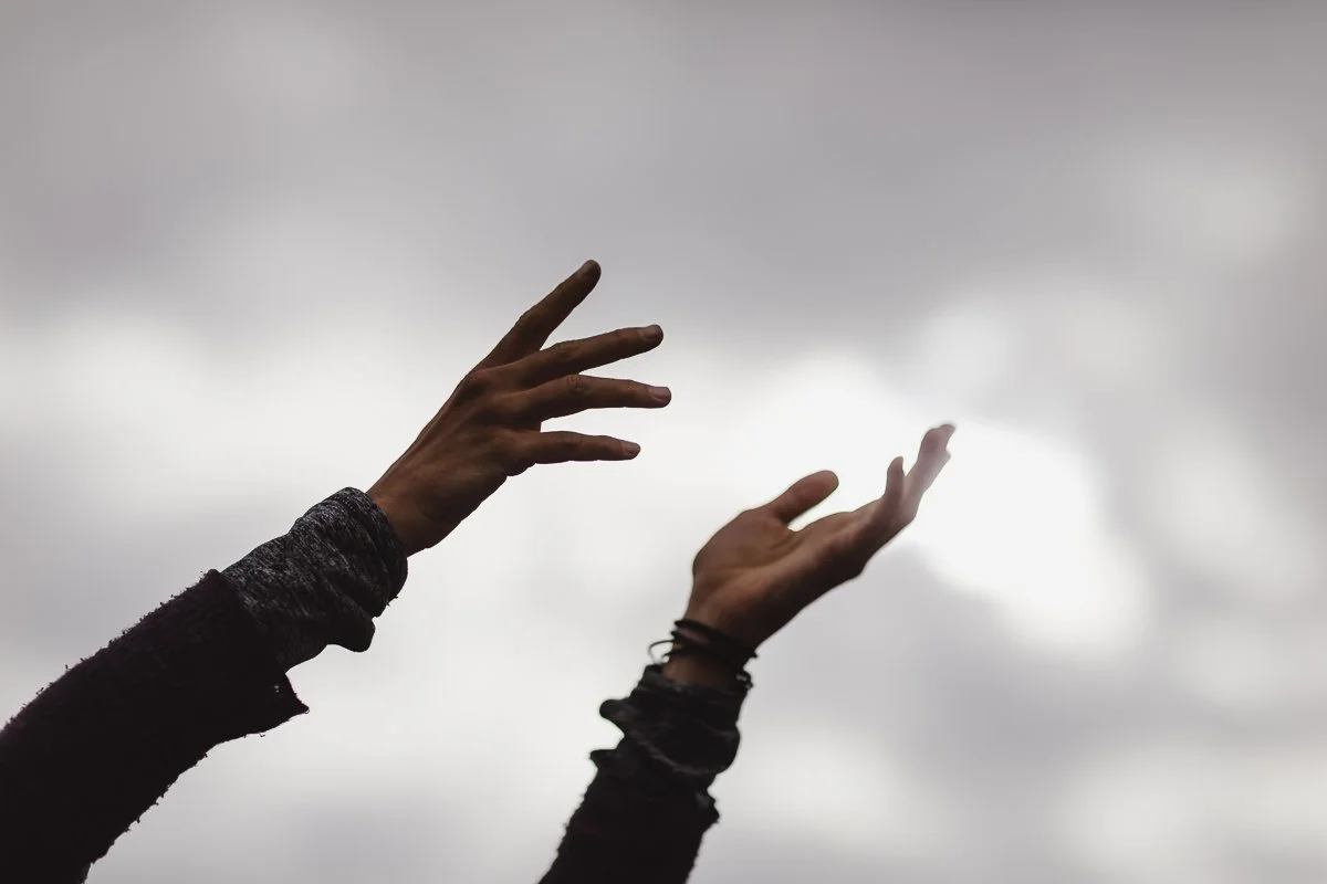 Two hands reaching upward against a cloudy sky.