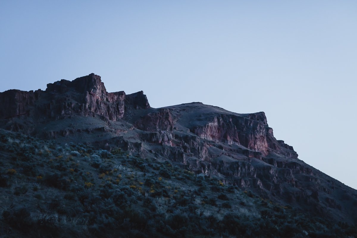 A mountain with steep, rugged slopes under a clear sky at dusk.
