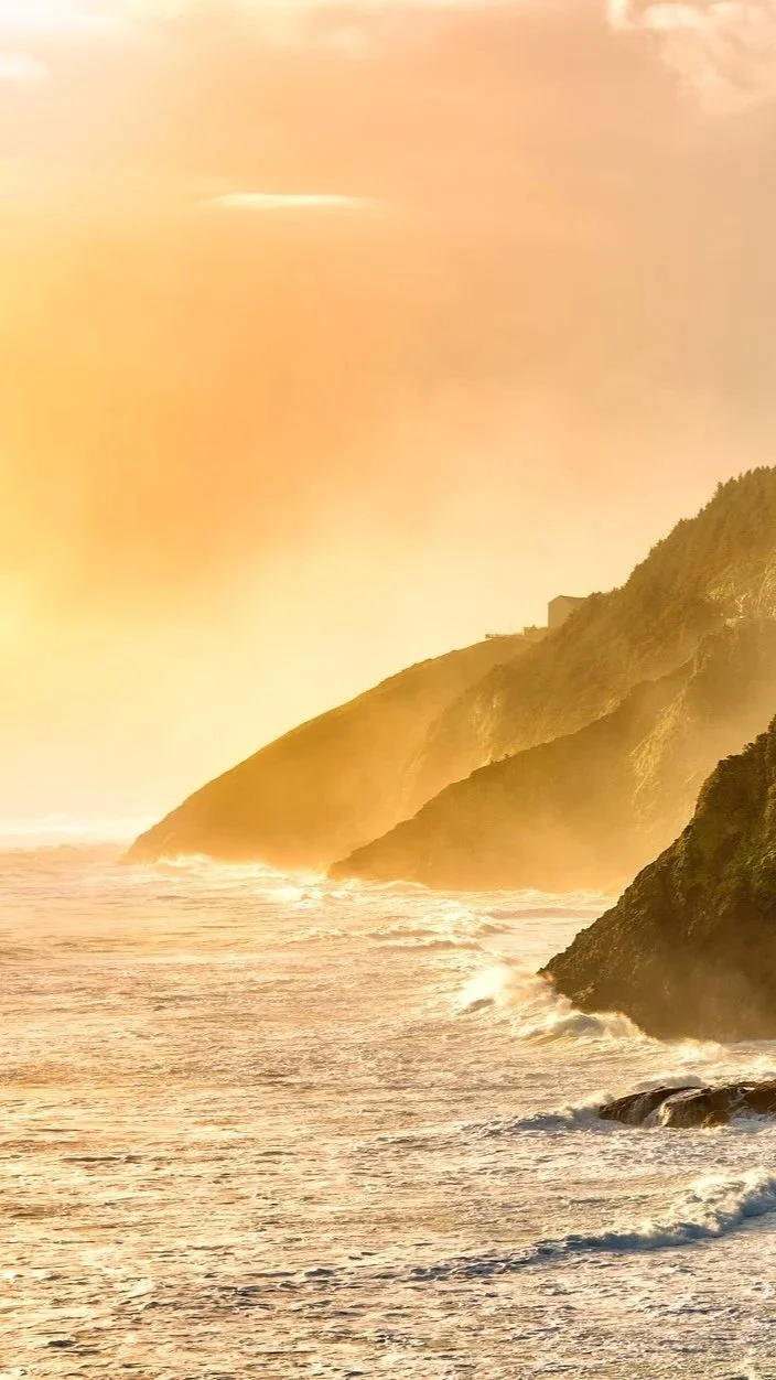 Sunset over ocean with waves crashing against cliffs