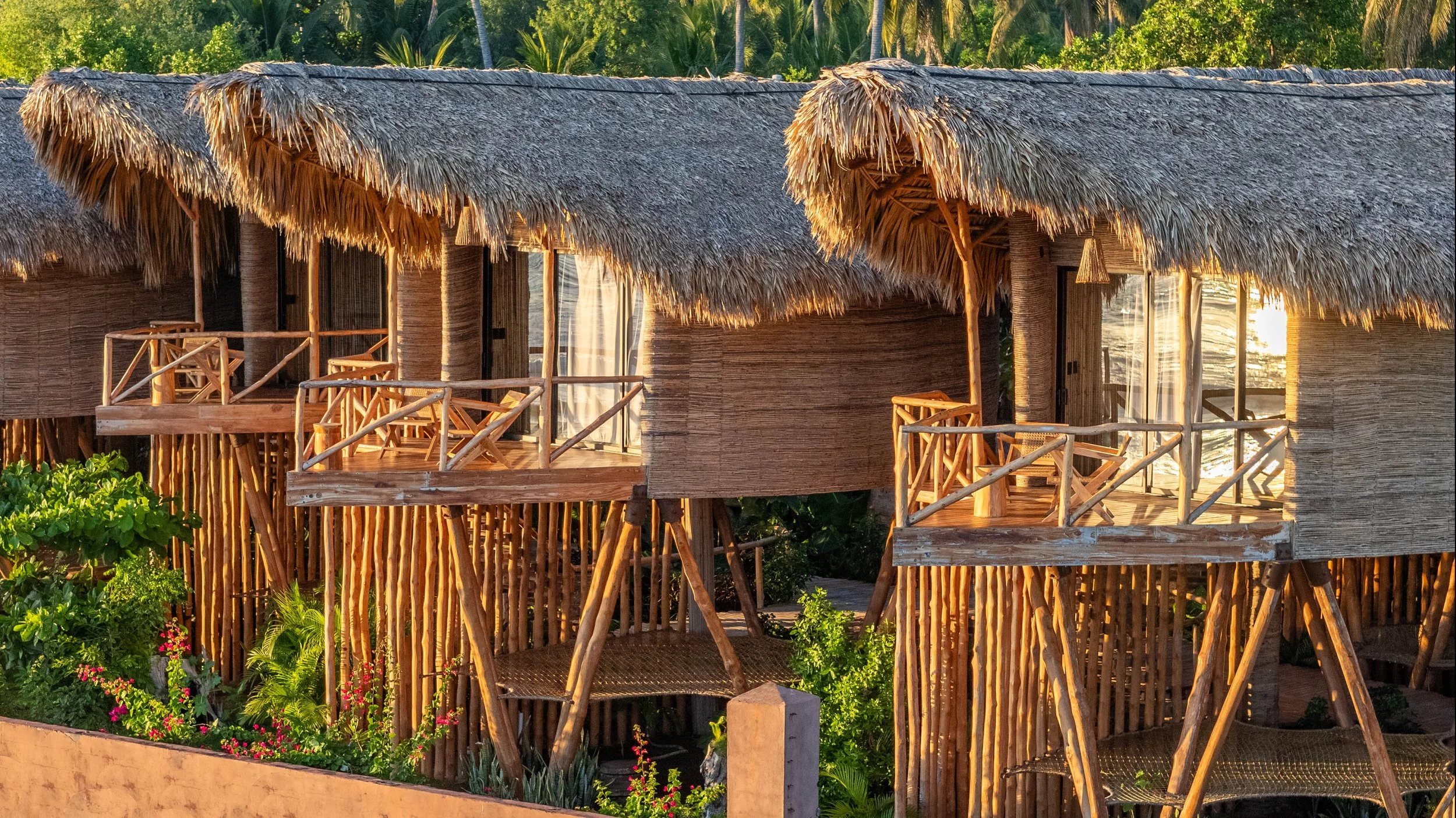 Overwater bungalows with thatched roofs and wooden balconies, surrounded by lush greenery in a tropical setting.
