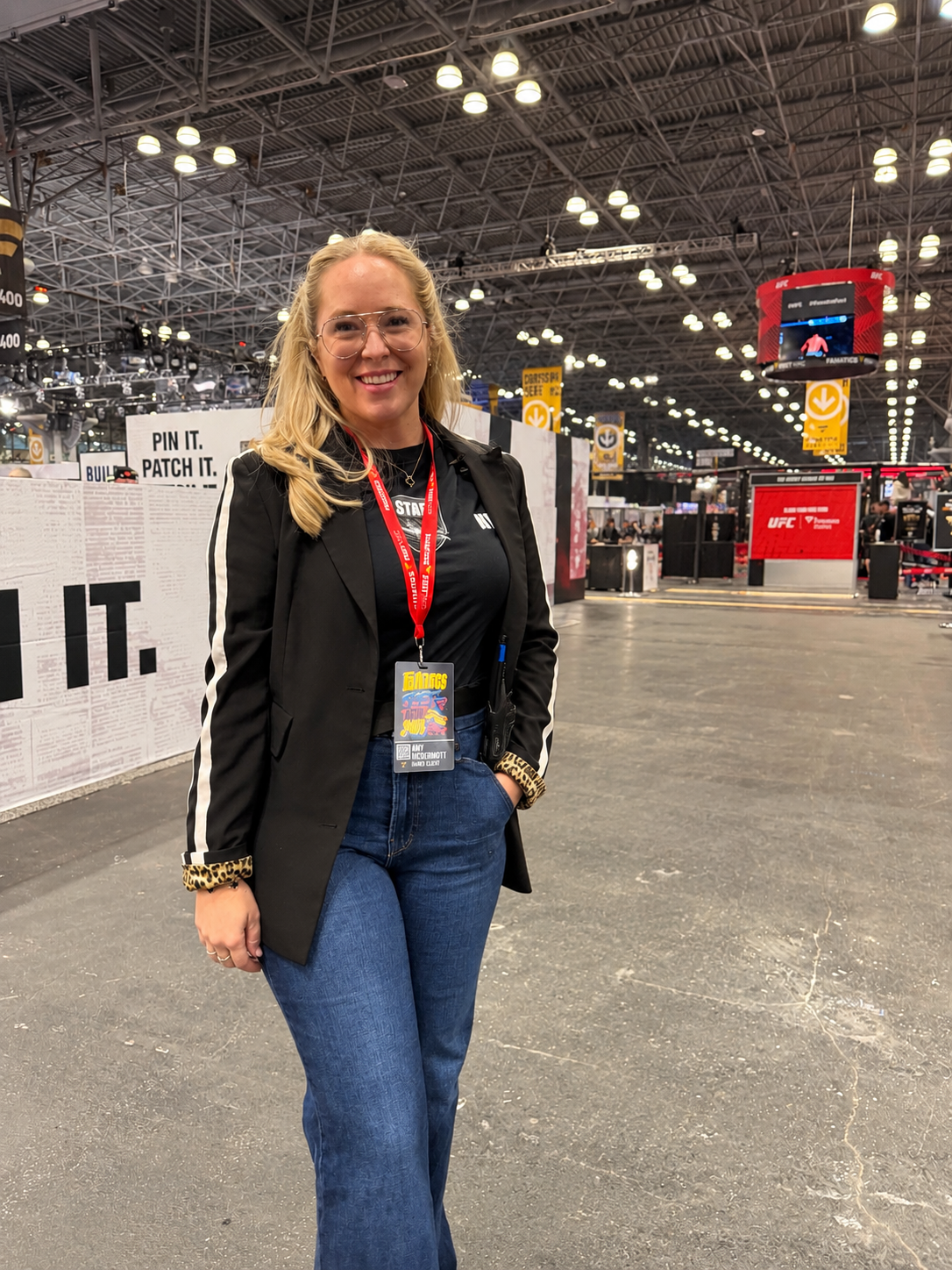 A woman wearing a Fanatics Fest red lanyard with a badge, standing inside Javtis Center at FanaticsFest