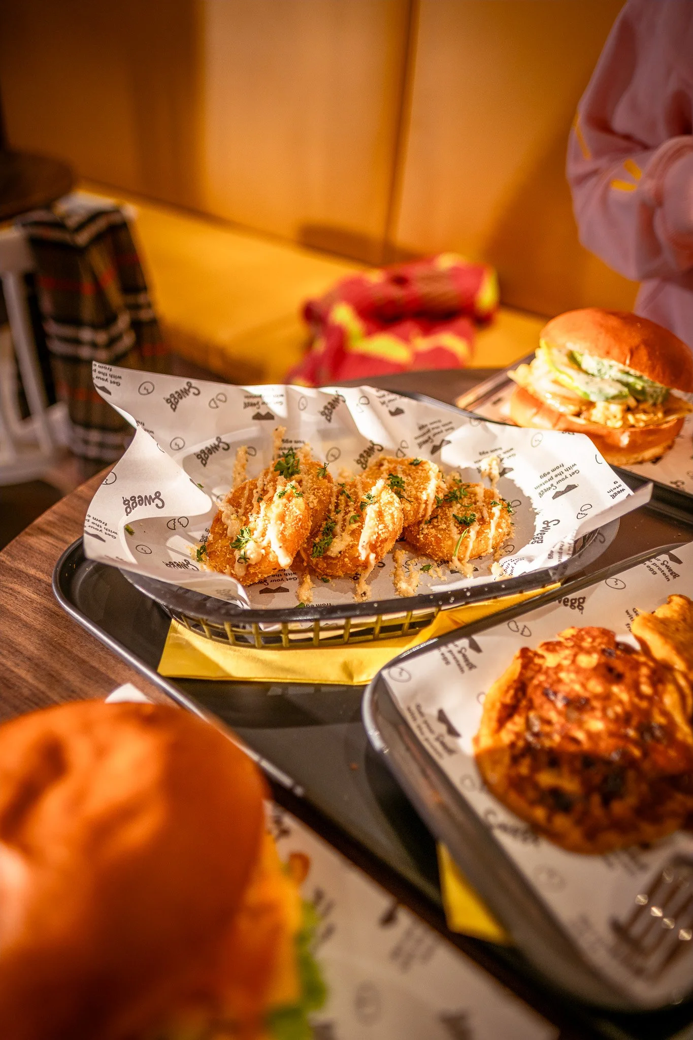 Bord met verschillende gefrituurde hashbrowns en Pompoen Pannekoeken op papieren onderleggers met het logo 'Swegg Sandwich' in een restaurant.