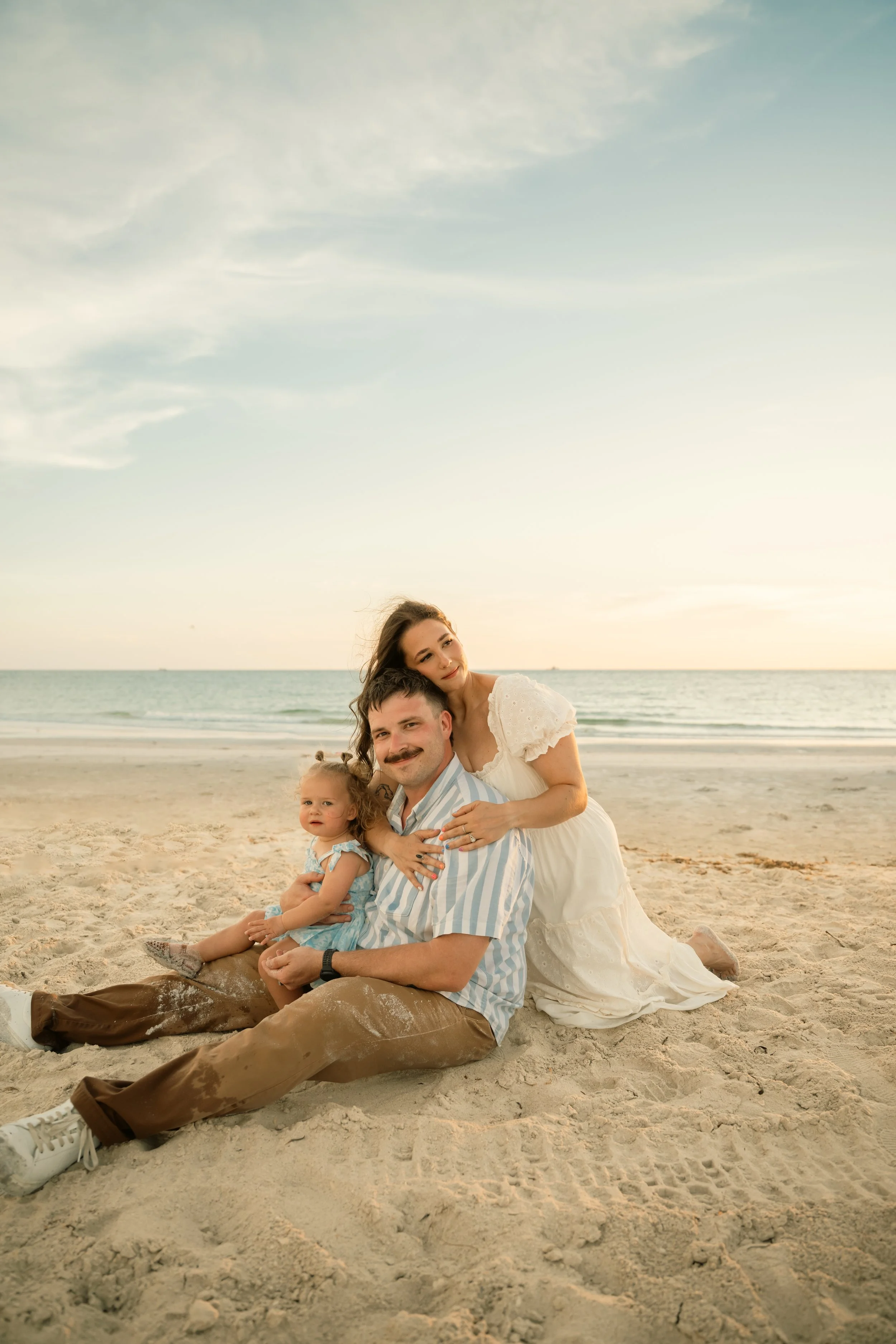 Family of three smiling together on Clearwater Beach with the ocean in the background
