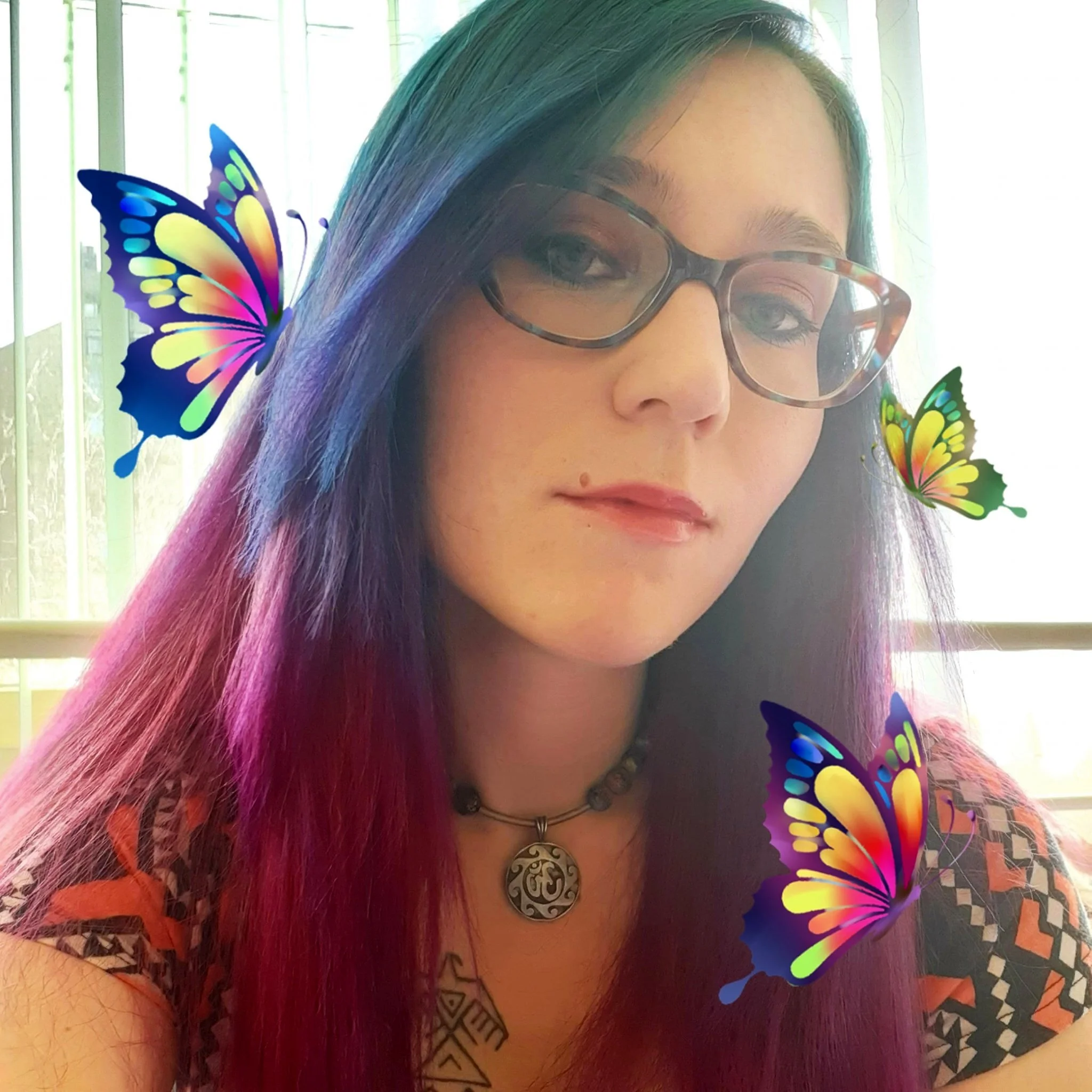 Person with colorful hair and glasses, wearing a pendant necklace, surrounded by digital butterflies.