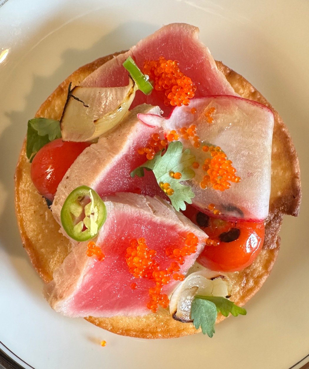 Appetizer with slices of watermelon radish, cherry tomatoes, chili pepper slices, microgreens, and orange fish eggs on a toasted bread base.