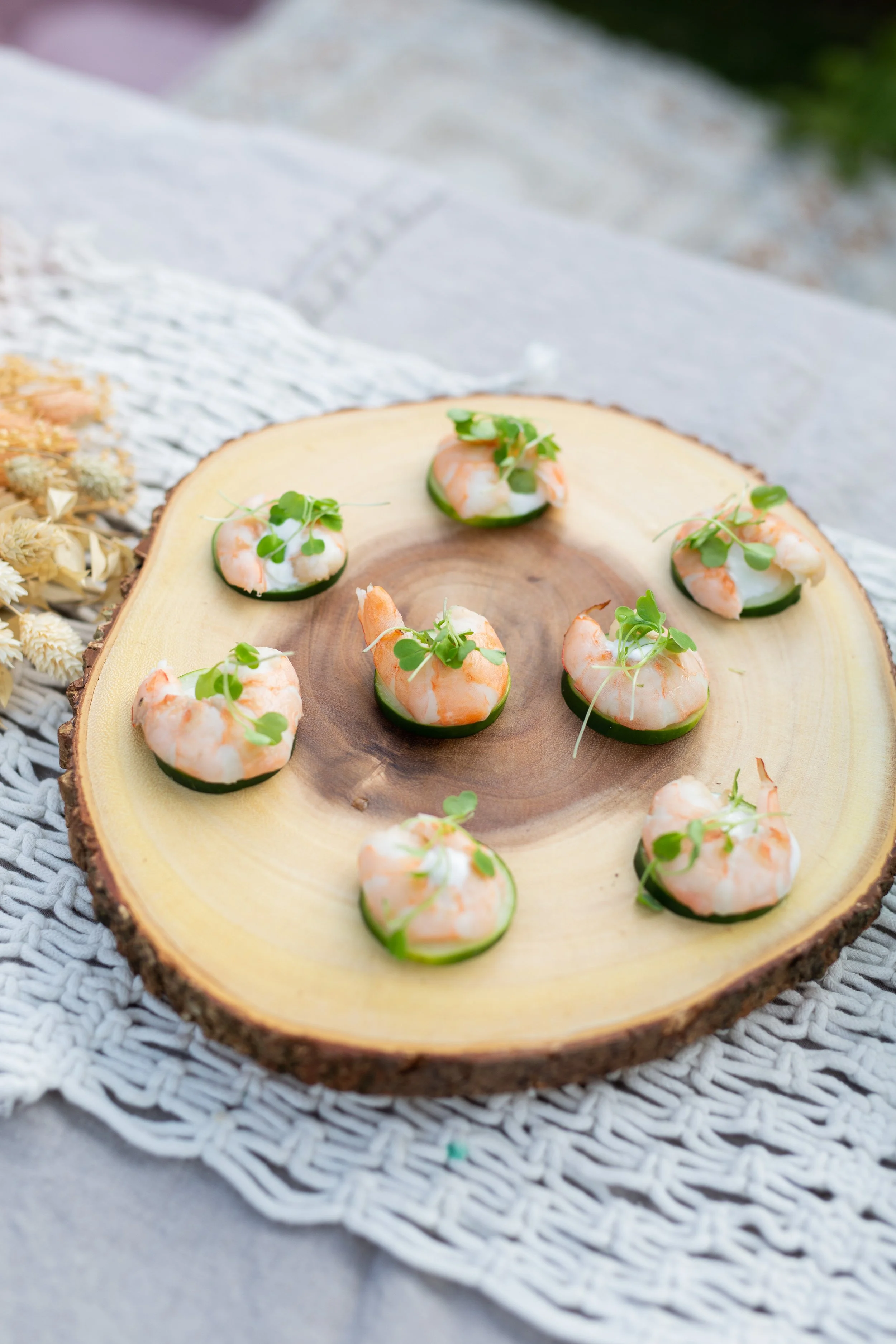 Shrimp and cucumber canapés garnished with microgreens on a wooden serving platter.