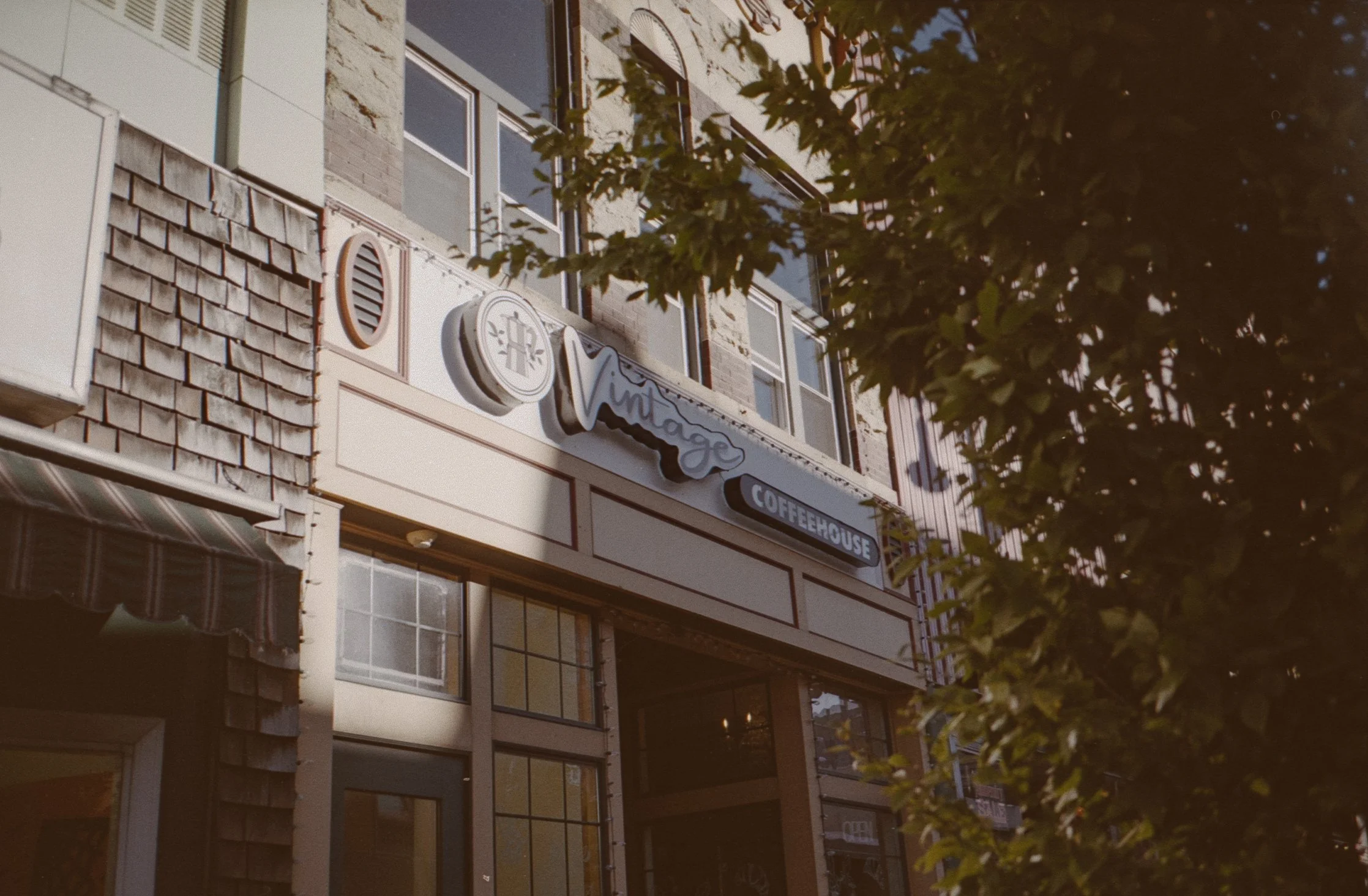Exterior of a vintage coffeehouse with a prominent sign and large windows, partially obscured by tree branches.
