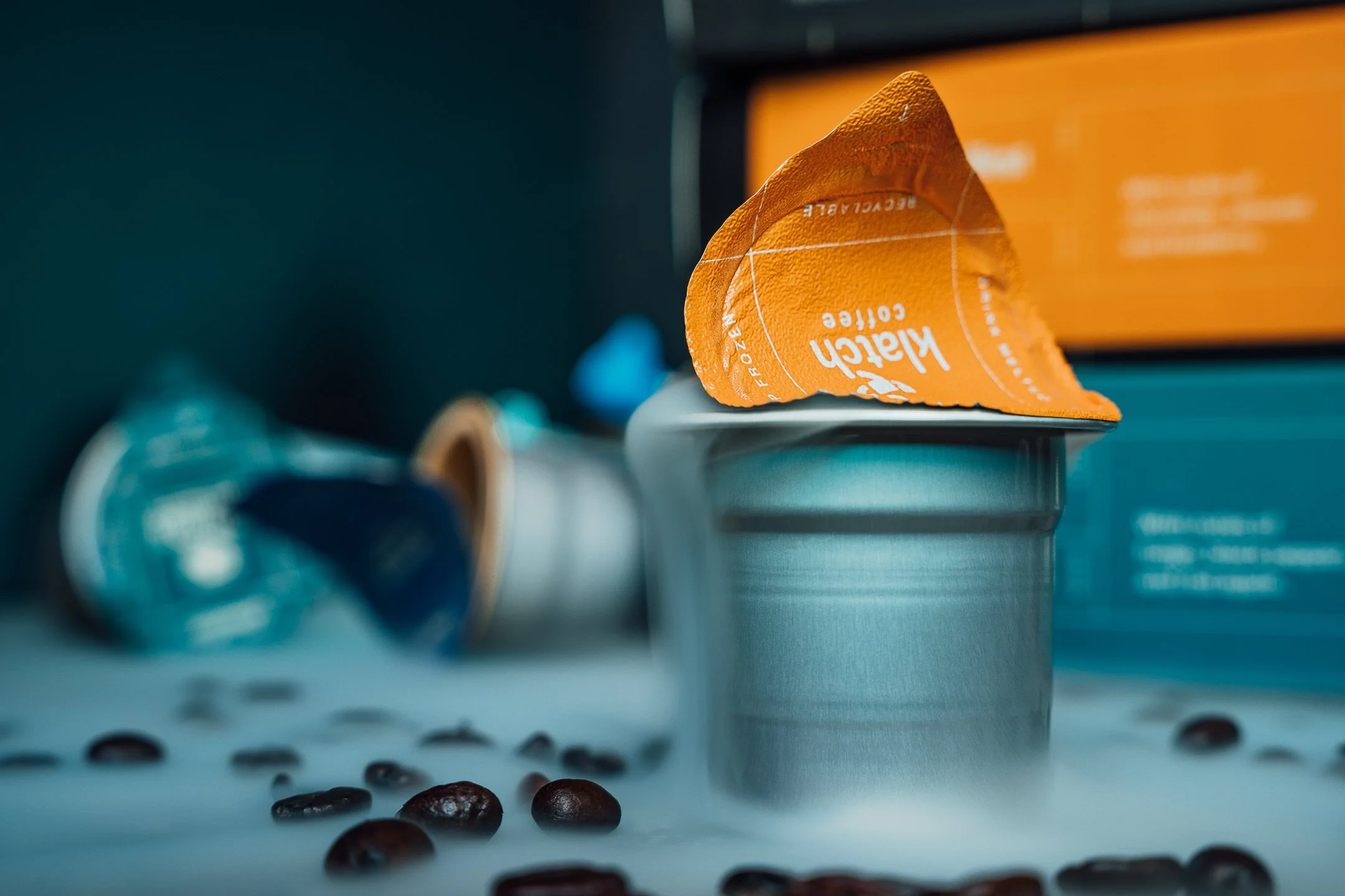 Cometeer pod with dry ice pouring over the side. Image features coffee beans, Cometeer boxes and additional pods in the background.