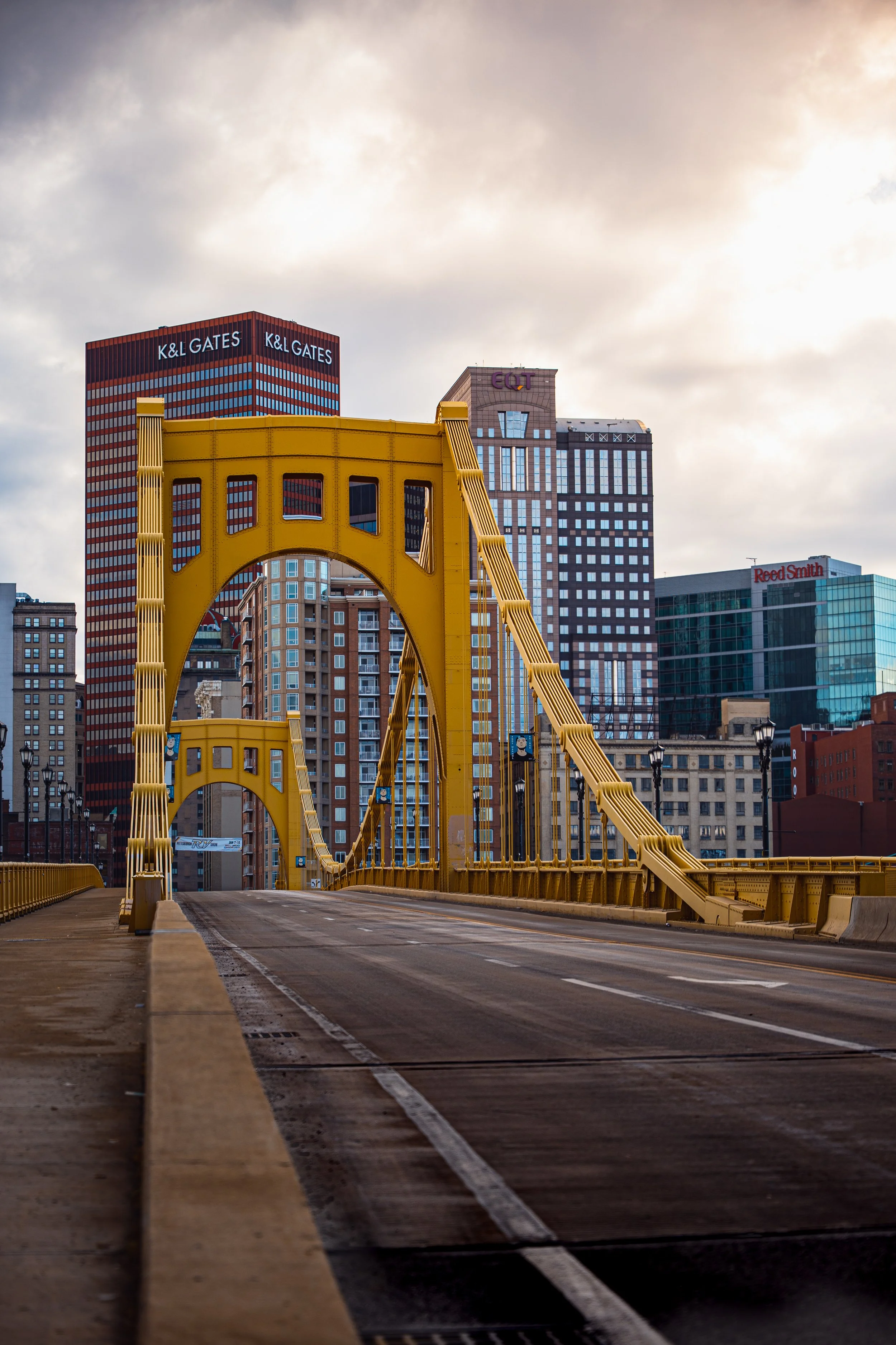 Downtown Pittsburgh bridge with yellow suspension cables and city skyline in the background.