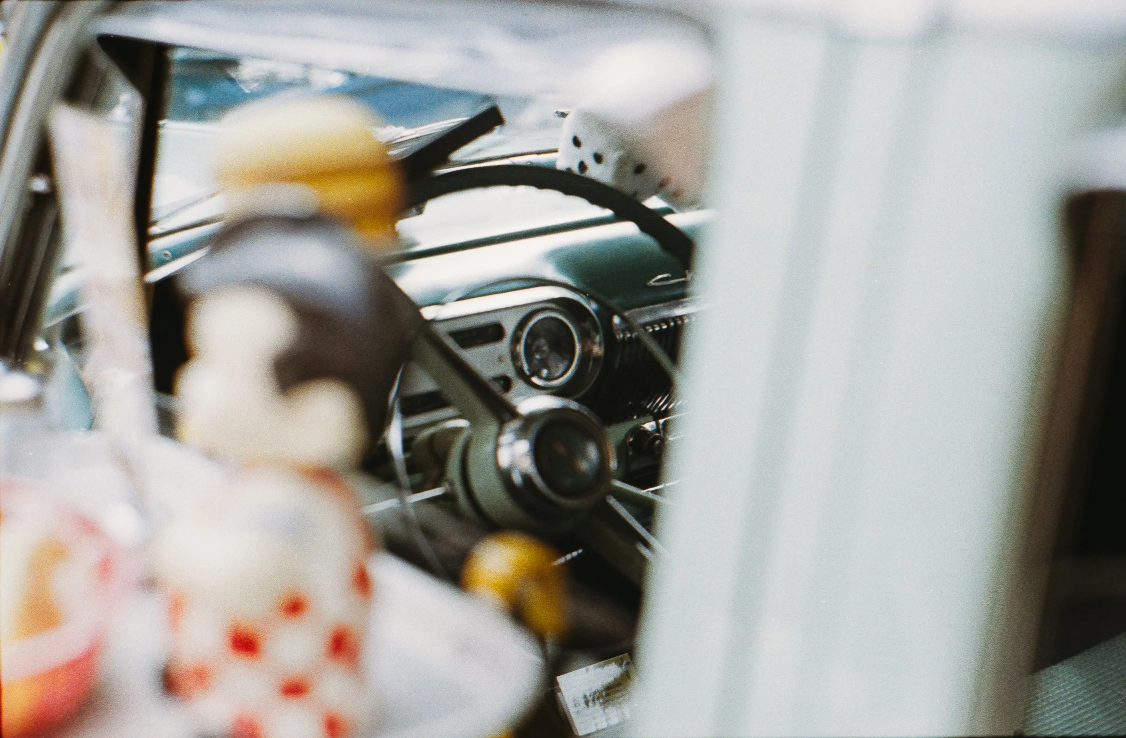 Close-up of vintage car dashboard with dials, steering wheel, and a blurred doll with polka-dot clothes in the foreground.