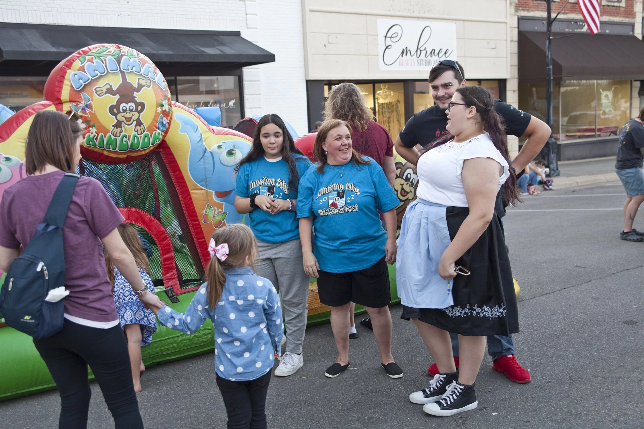 People gathered around a colorful inflatable bounce house at a street fair, with children and adults engaging and smiling.