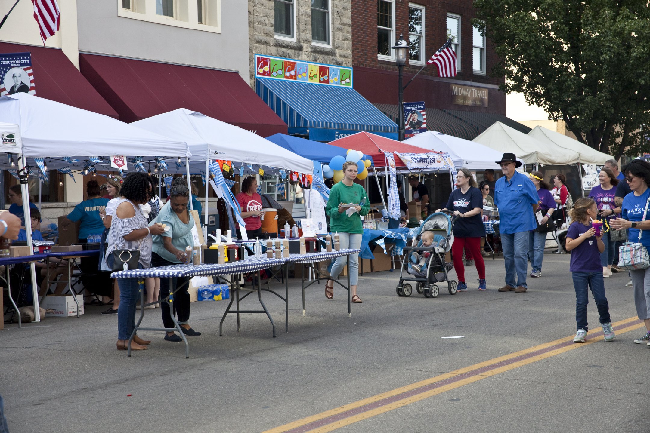People shopping at an outdoor street fair with vendor tents, balloons, and patriotic decorations in a small town.