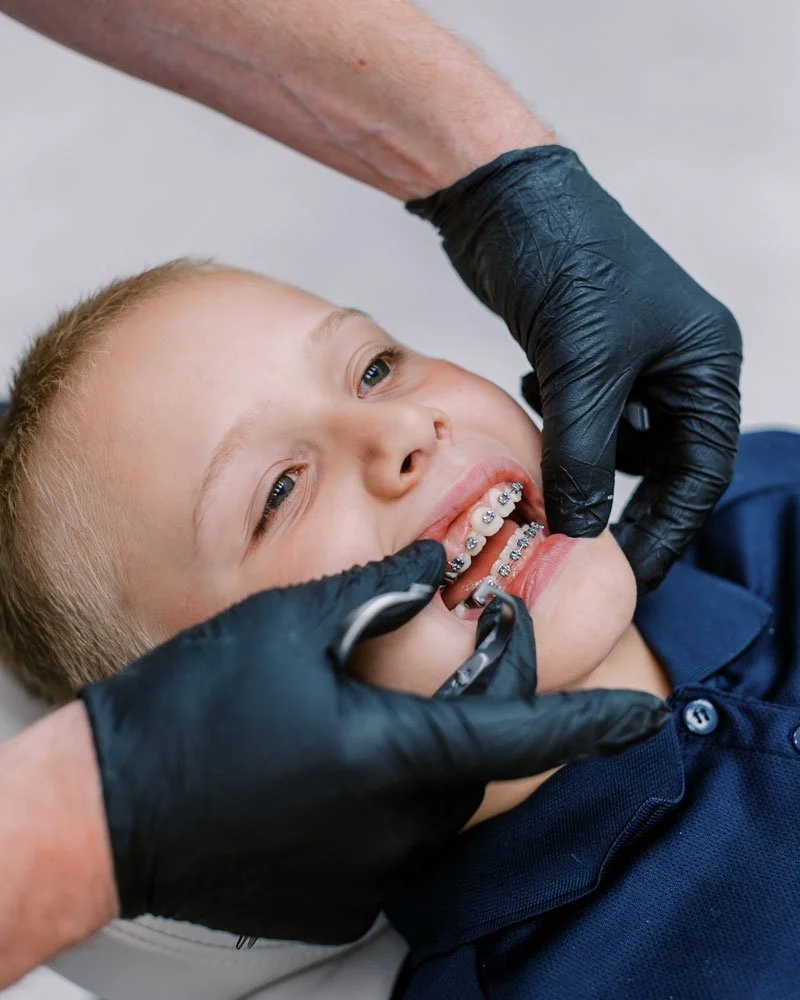 A young boy with braces getting a orthodontic check-up from an orthodontist wearing black gloves.