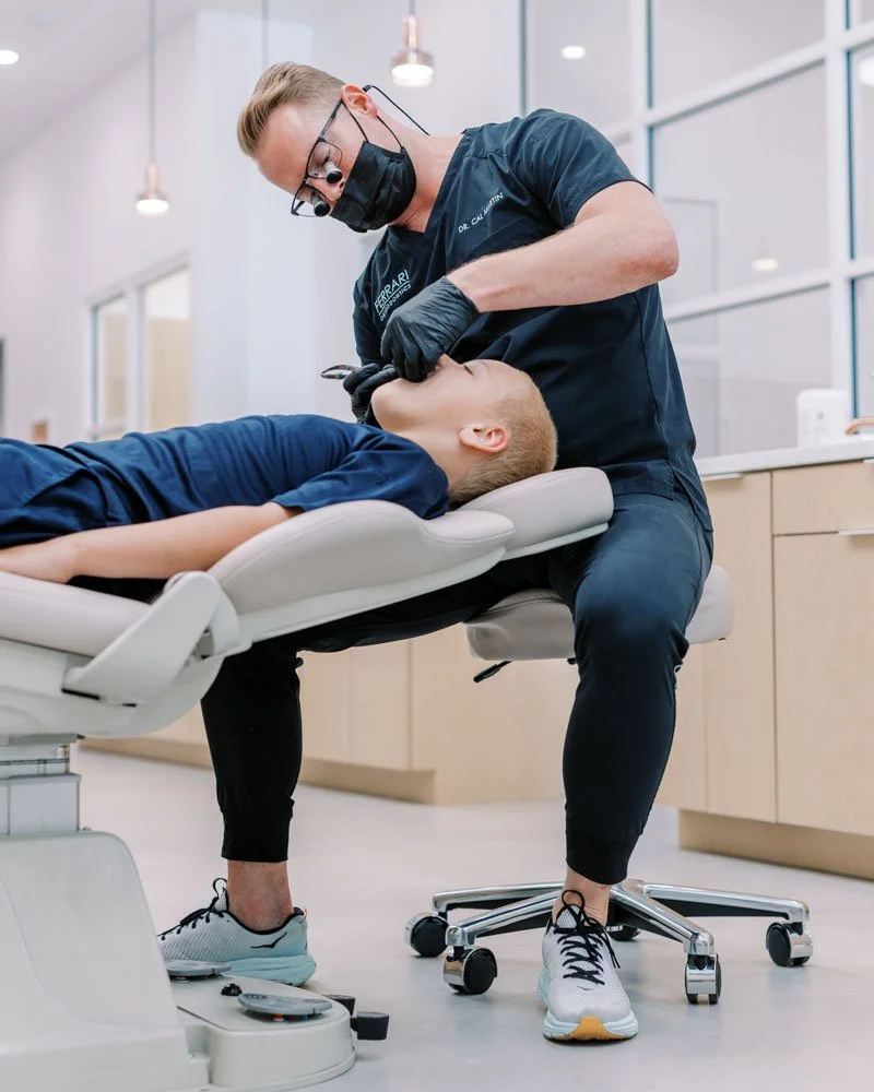 Orthodontist performing a dental examination on a young boy lying in a dental chair, in a modern dental office.