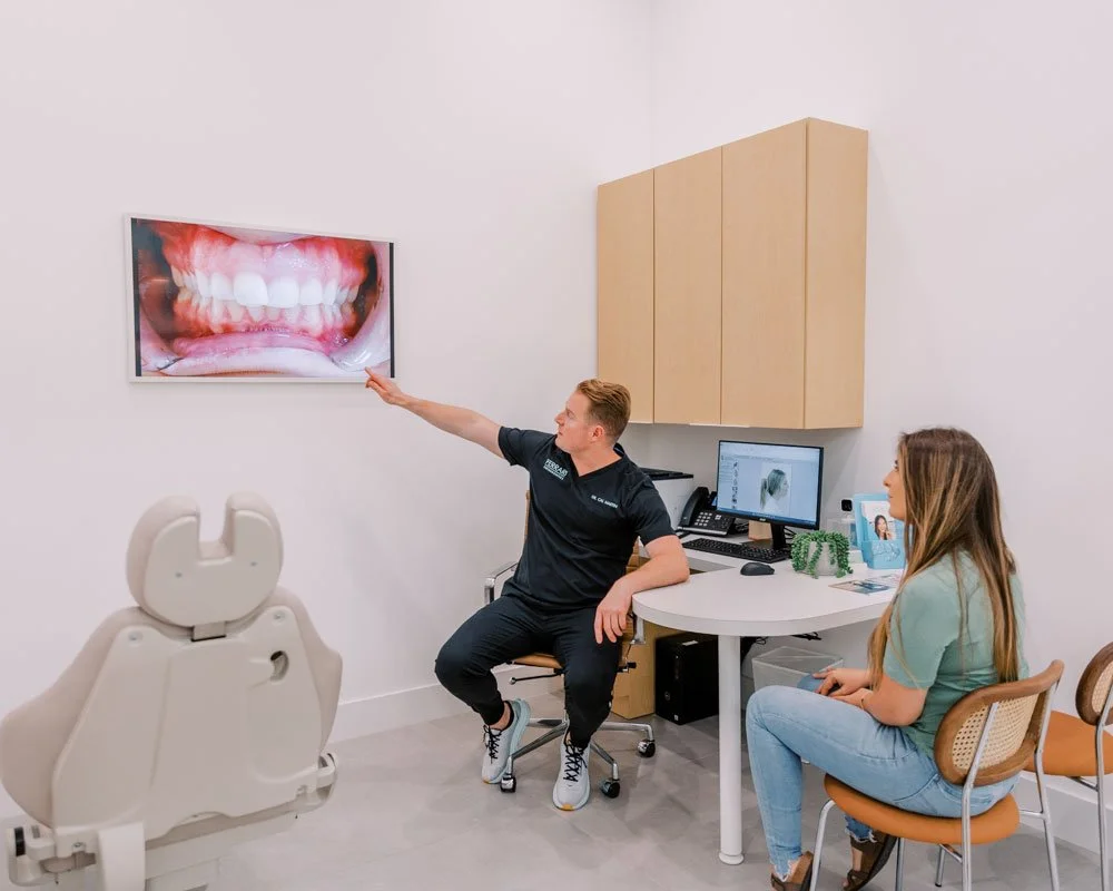 Dentist and patient in consultation, with a large dental image on the wall showing teeth and gums.