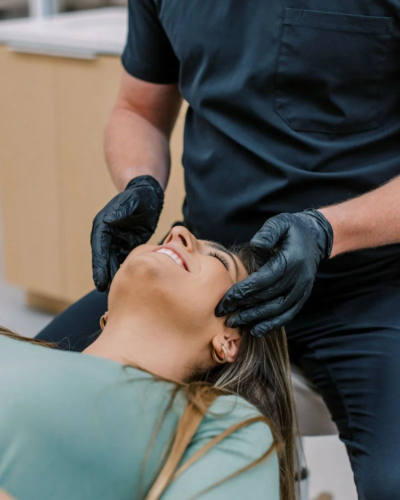 A woman laying on a dental chair receiving dental care from an orthodontist wearing black gloves