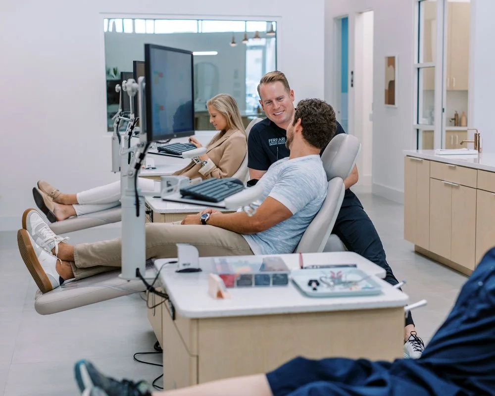 A smiling orthodontist talking to a seated male patient in a modern dental clinic.