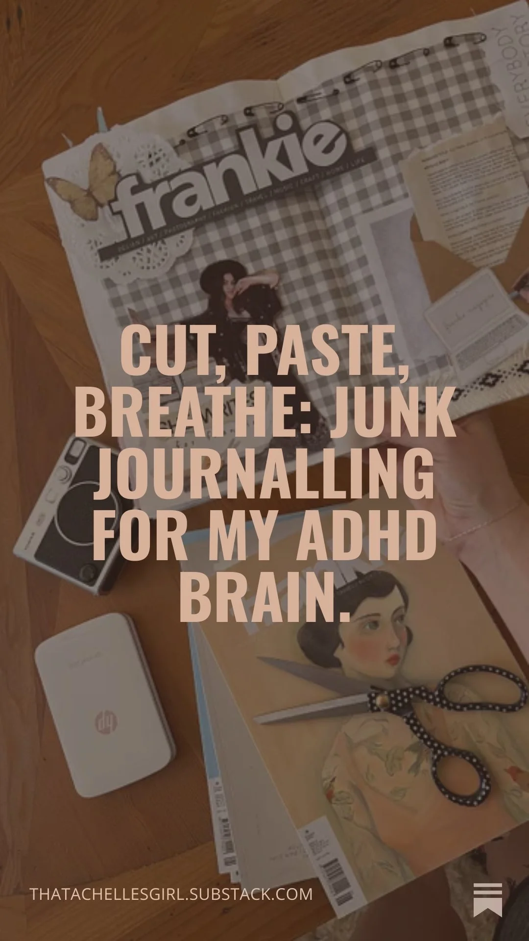A table with a magazine, a Polaroid camera, a pair of black scissors with white polka dots, a white HP printer, and a notebook featuring a woman's portrait. 