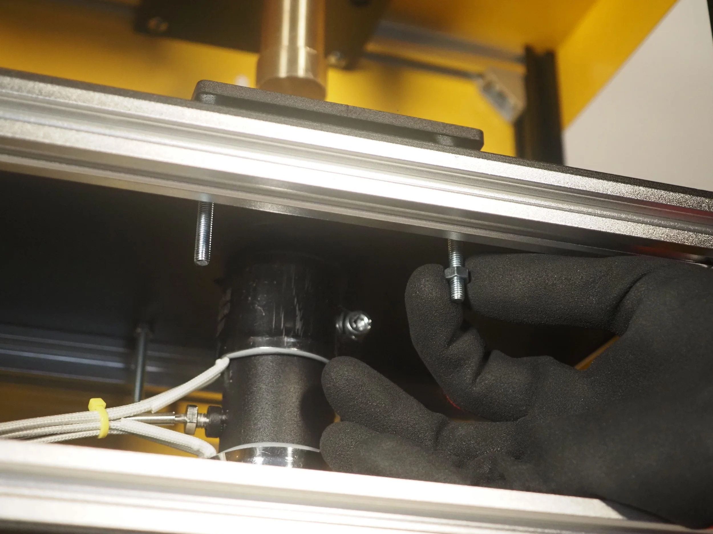 Close-up of a motorized part with metallic frames, black components, white wires, and a black-gloved hand adjusting a screw.