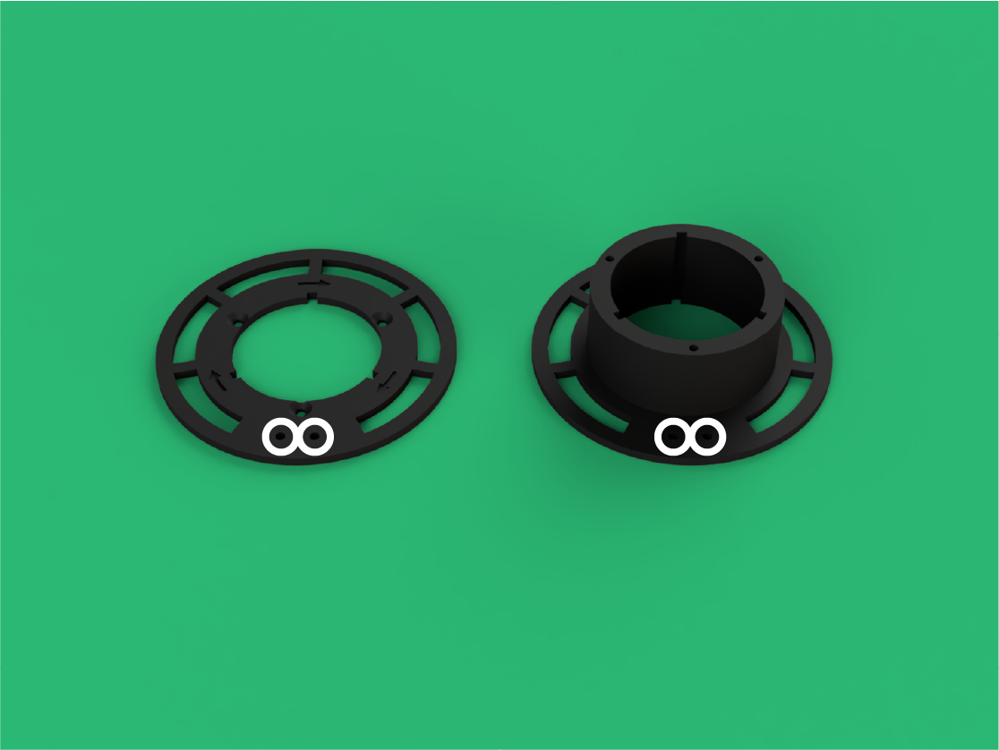 Two black circular plastic components with white eye-like markings on a green surface.