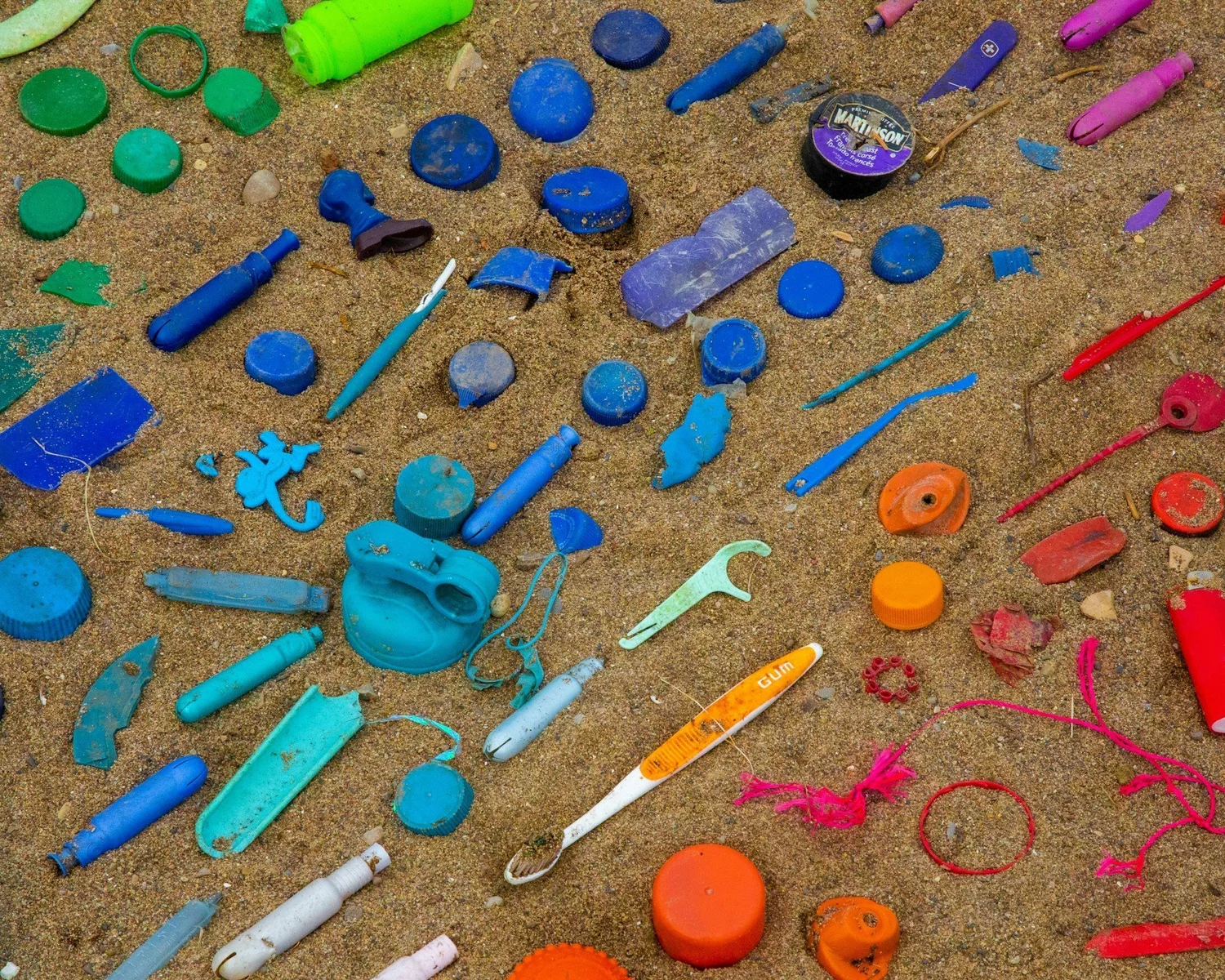 Colourful plastic toys and debris scattered on sandy ground.