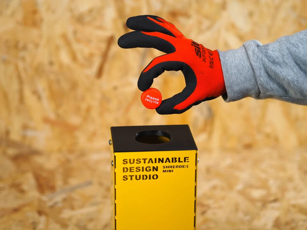 A gloved hand feeding plastic into a Shredder Mini V2 on a workbench.