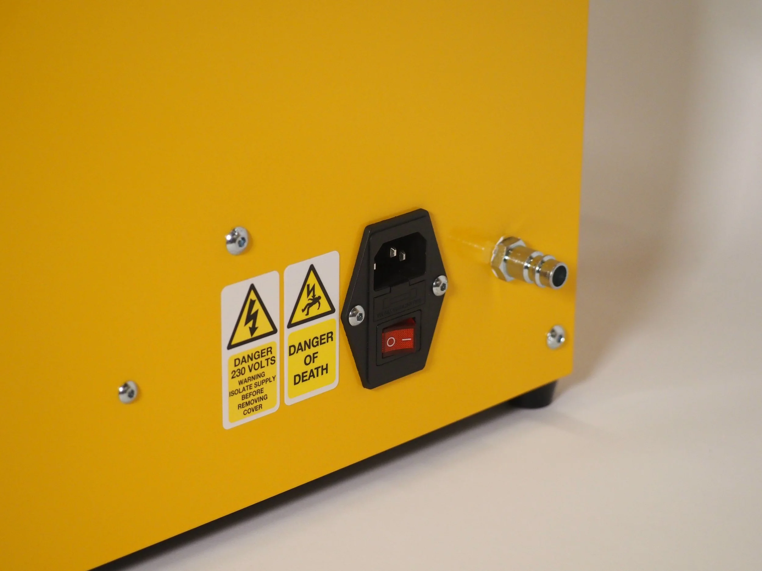 Close-up of a yellow electrical device with warning labels, a power switch, a power outlet, and a connector