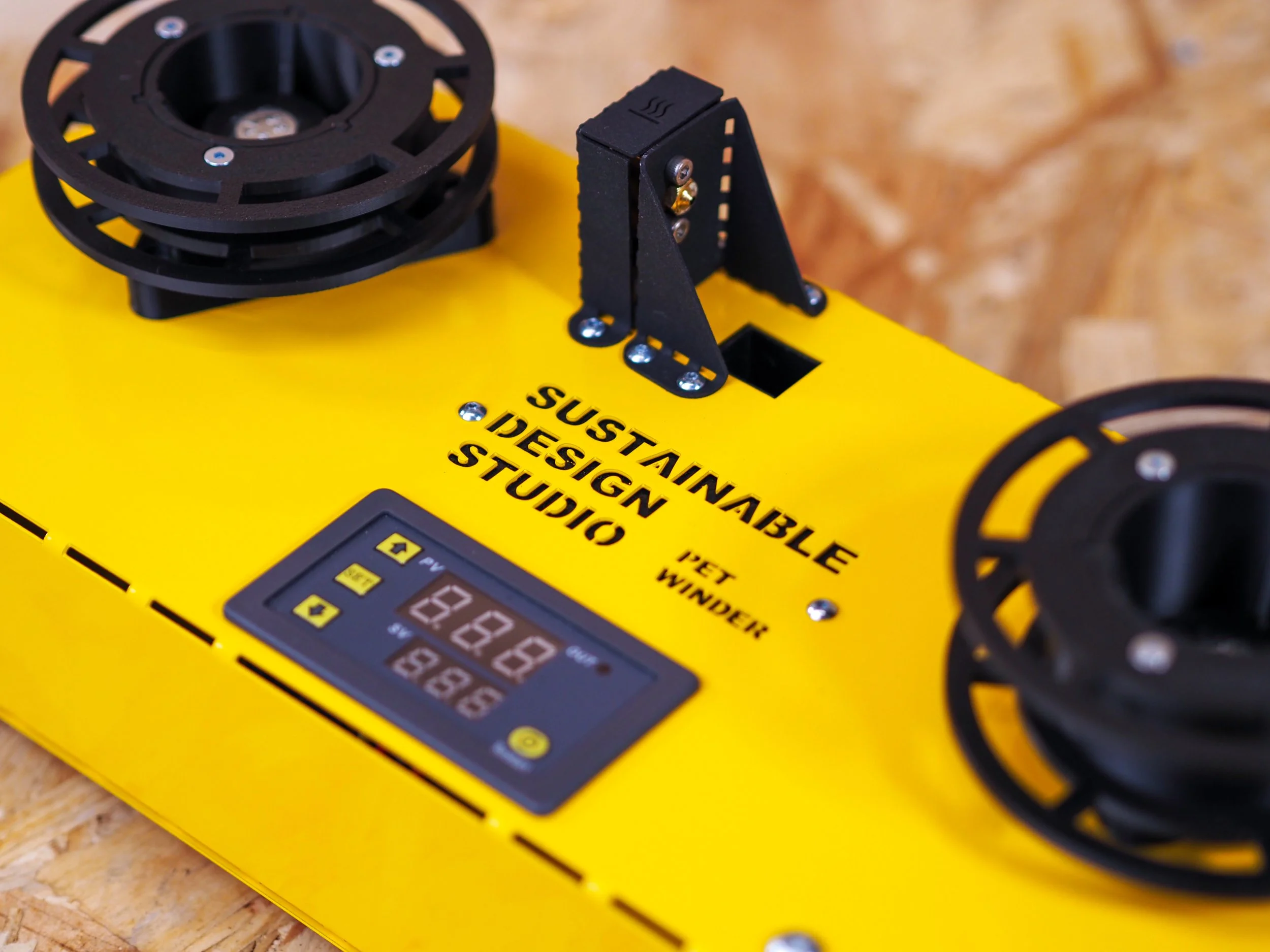 A yellow robot kit with black circular robotic wheels, an LCD display, and an adjustable arm, with the text 'SUSTAINABLE DESIGN STUDIO' printed on it.