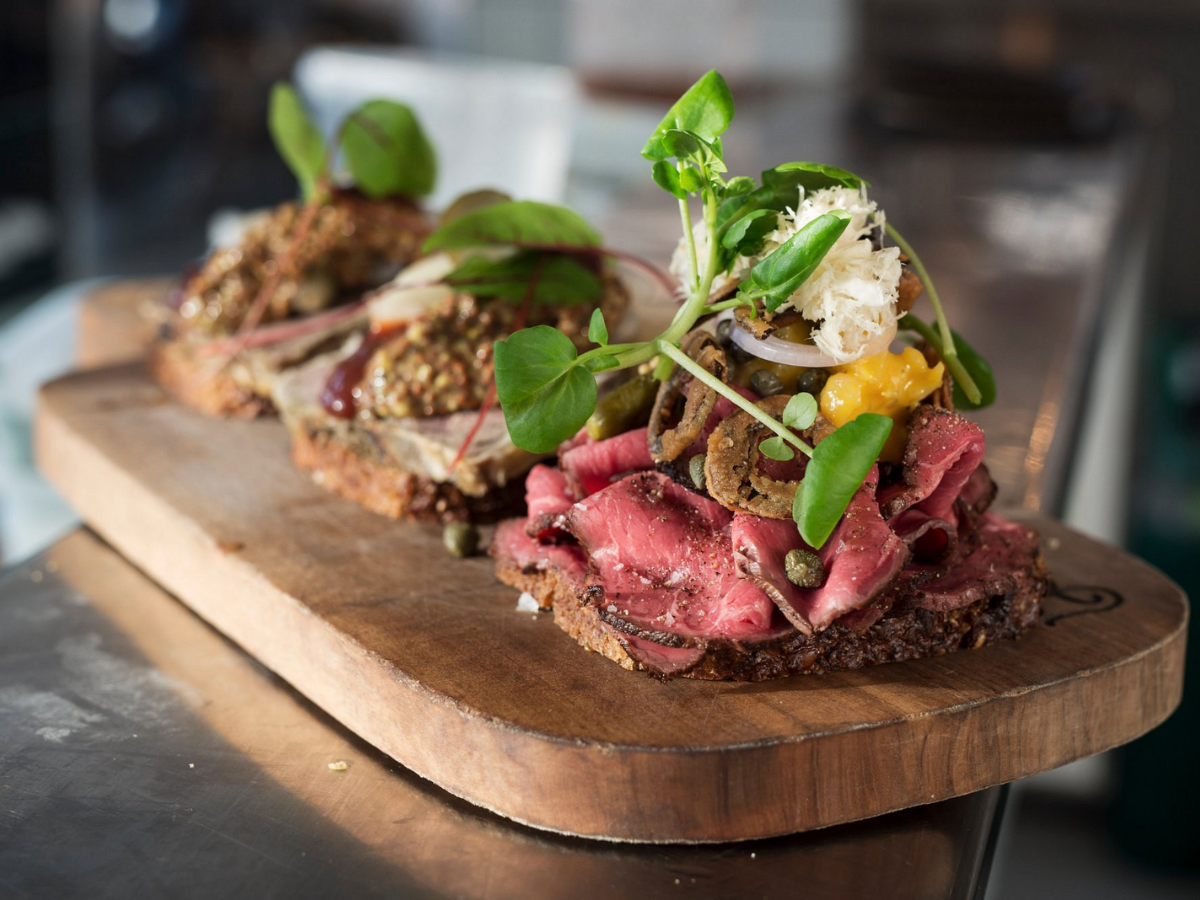 Tre stykker smørrebrød med forskellige topping på en træplade.