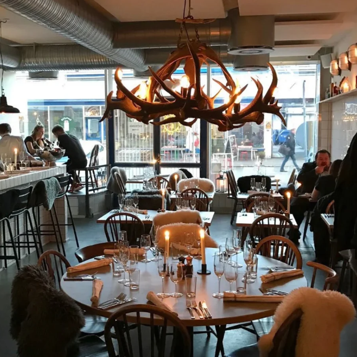 Spiselokalet hos Restaurant Fleisch i Kødbyen med dækkede borde, levende lys og en stor gevirlampe.