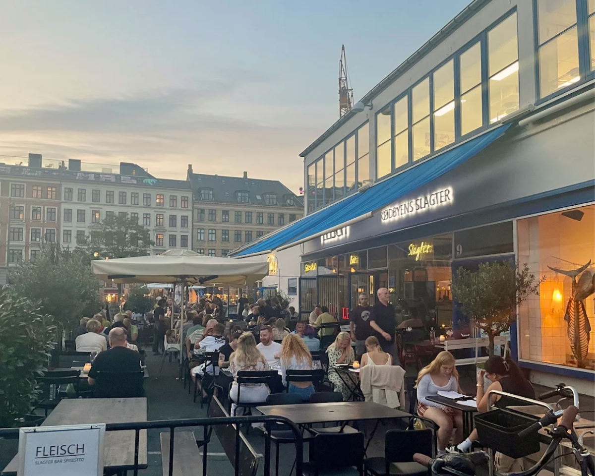 Udeservering med mange mennesker i København, café med skriftet 'Kødbyens Slagter' på bygningen.