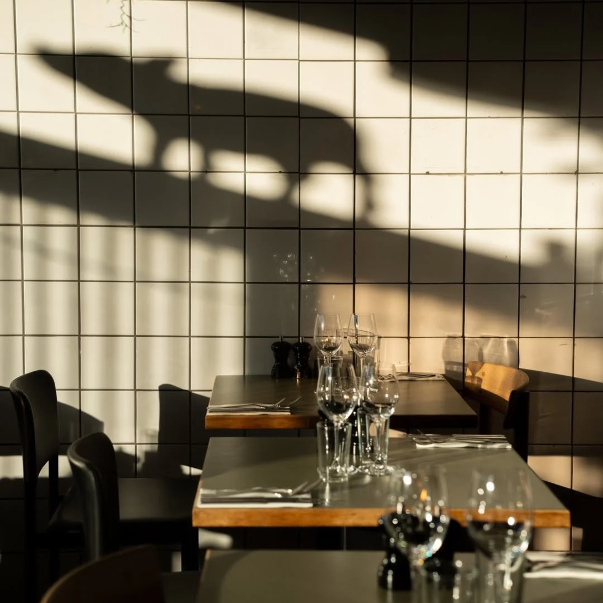 Sunlit tables and the shadow of a pig on the tiled wall at Restaurant Fleisch in Copenhagen’s Meatpacking District.