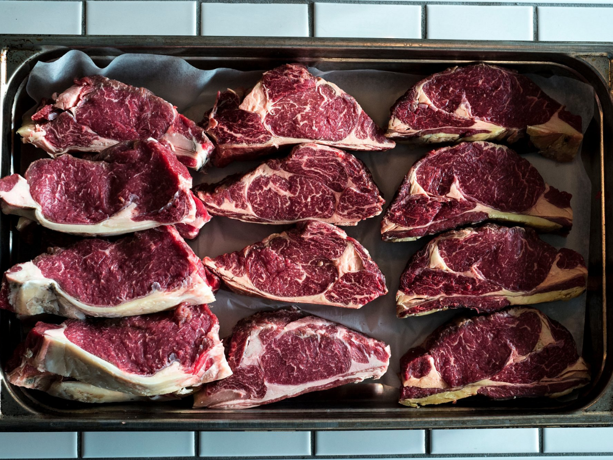 Udskårne ribeye bøffer lagt på en bageplade dækket med bagepapir.