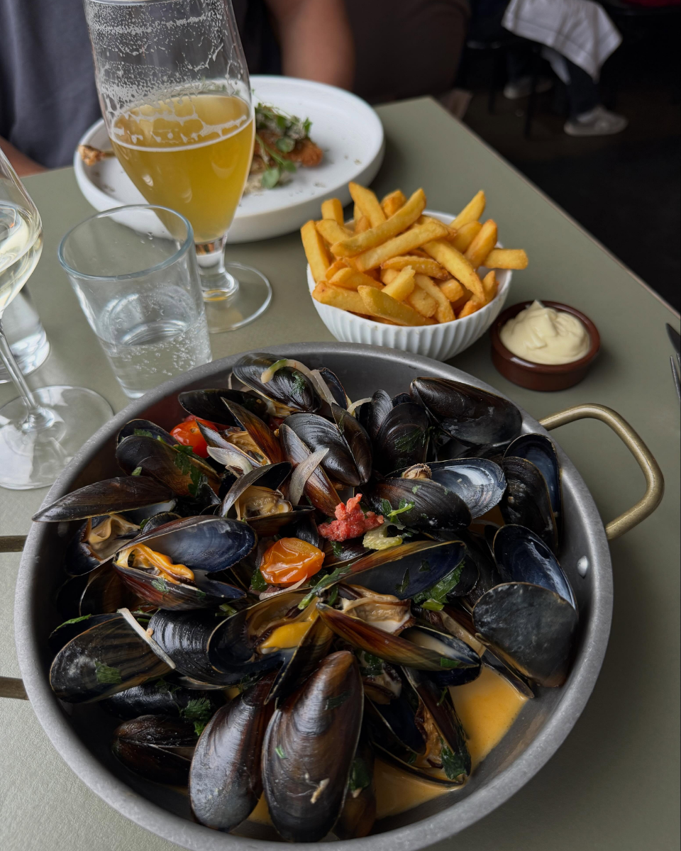 En skål med østers, en tallerken med pommes frites, og to glas med hvidvin. Der er også et glas med vand, en skål med mayonnaise, og en tallerken med mad i baggrunden.