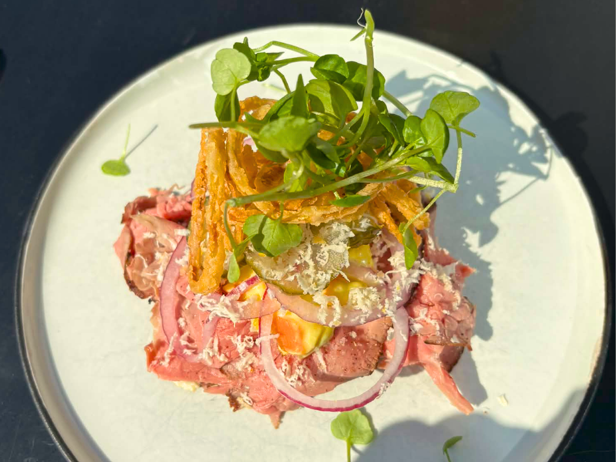 En tallerken med roast beef, toppet med radiser, sprøde løg, ost, og frisk microgrønt.