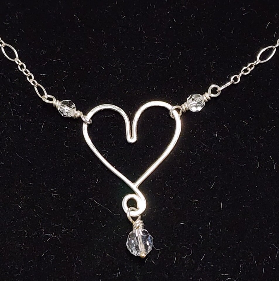 A sparkling shaped and soldered heart in .935 Argentium silver features a charm of faceted clear Swarovski Crystal below on a handmade ball pin. The centerpiece is wire-wrapped with smaller Swarovskis to a sterling long-and-short chain with a lobster
