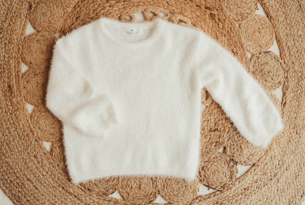 A white, fluffy sweater laid out on a woven, circular rug.