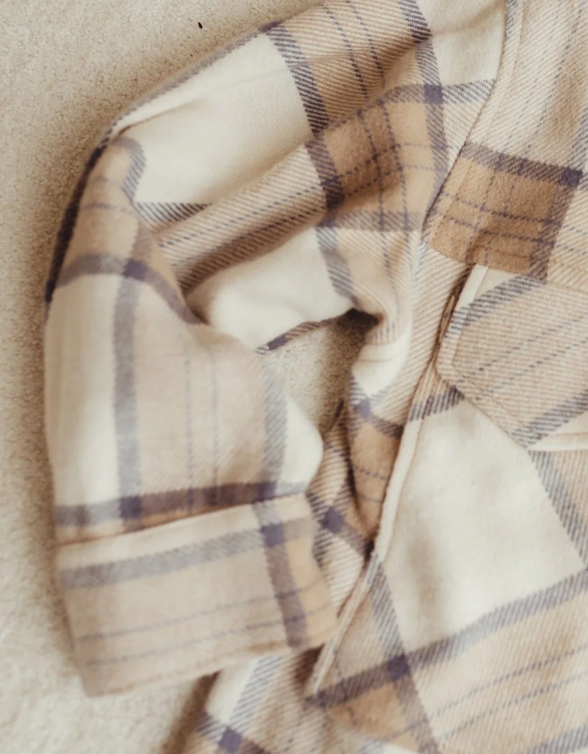Close-up of a beige and brown plaid shirt with a collar, lying on a beige carpet.
