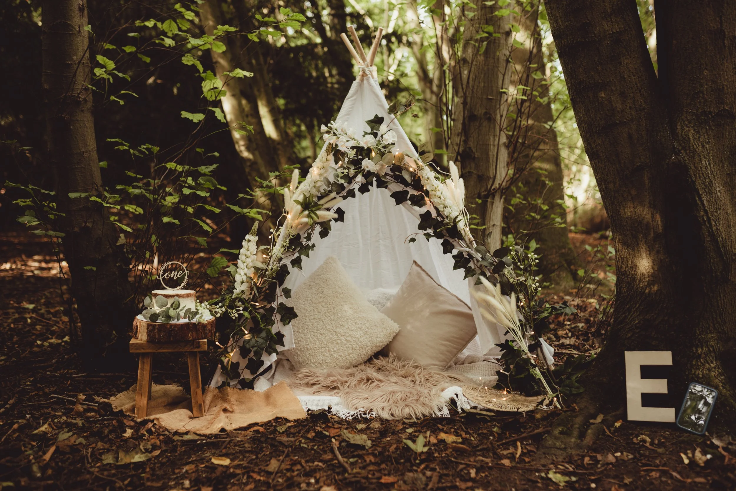 Woodland cake smash set up with a boho style tipi, fairy lights and soft blankets
