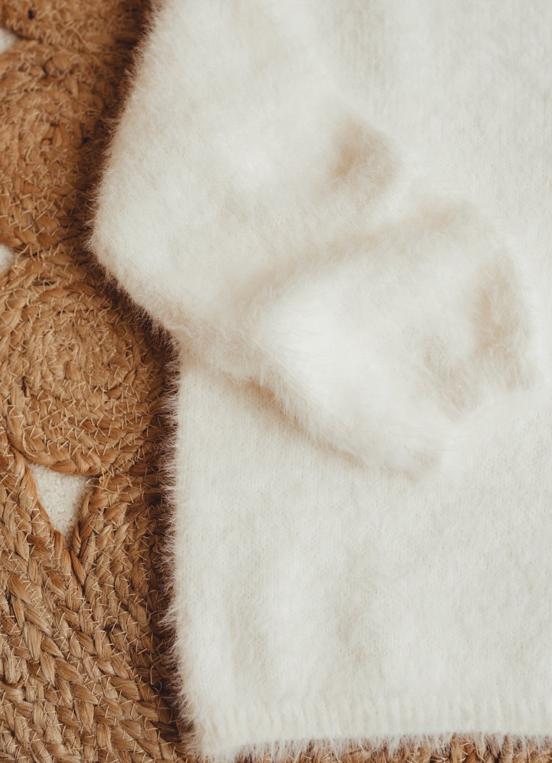 Close-up of a white fluffy fabric, possibly a wool or faux fur material, placed on a textured straw-colored woven surface.