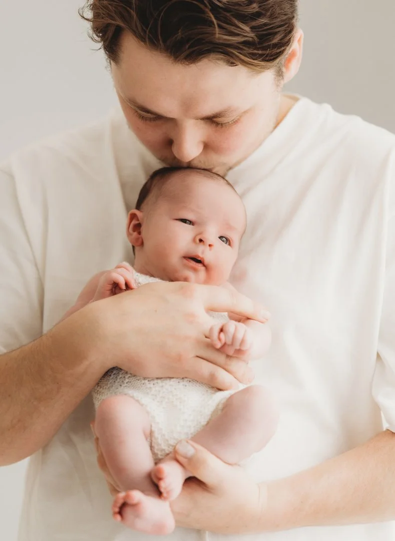 A Dad in white t shirt holding newborn close to his chest in a naturally posed photoshoot in Essex